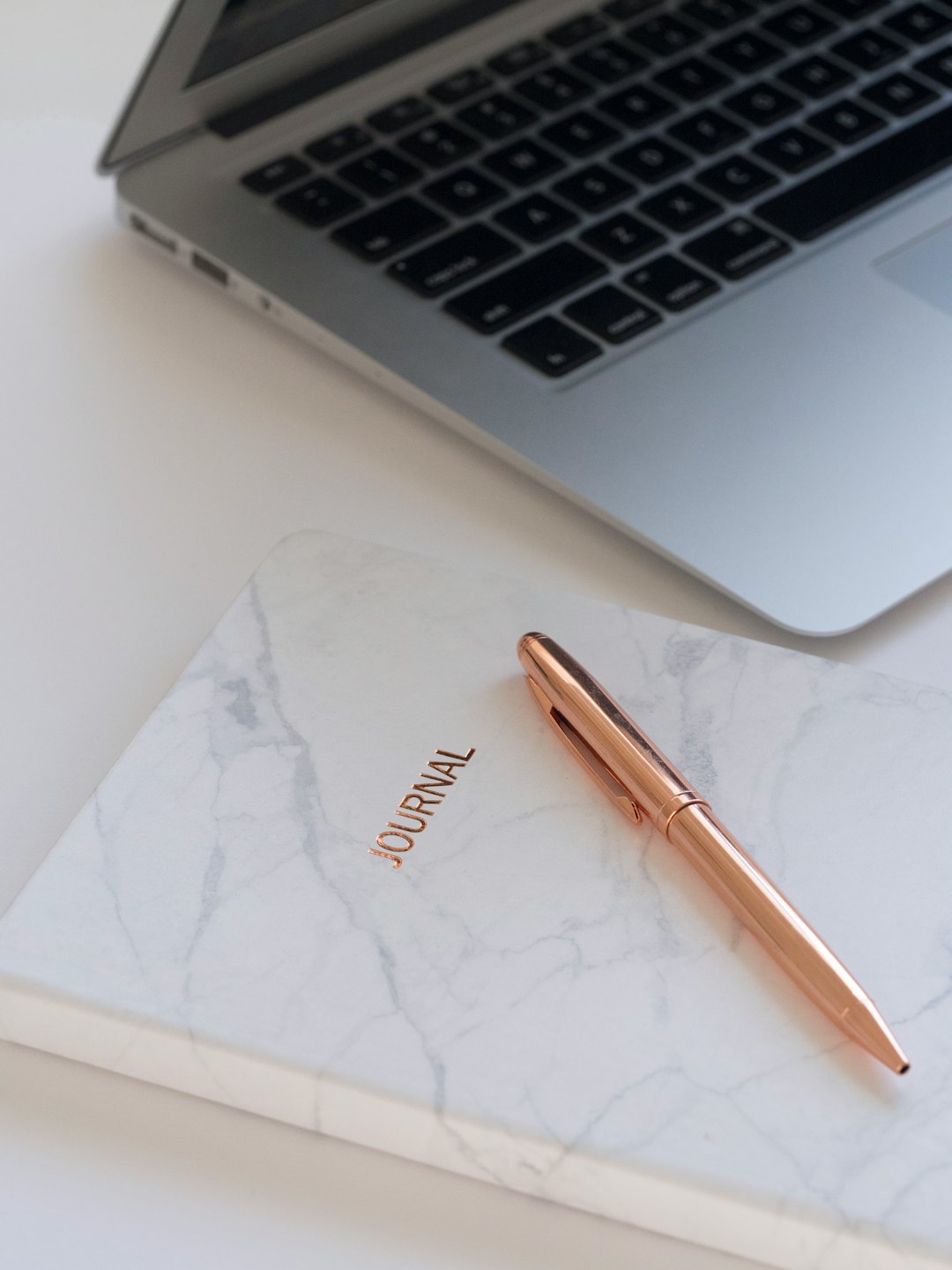 Minimalist desk with silver laptop, rose gold journal, and pen.