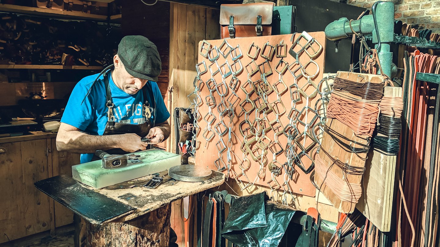 Craftsman working on metal buckle with small tool.