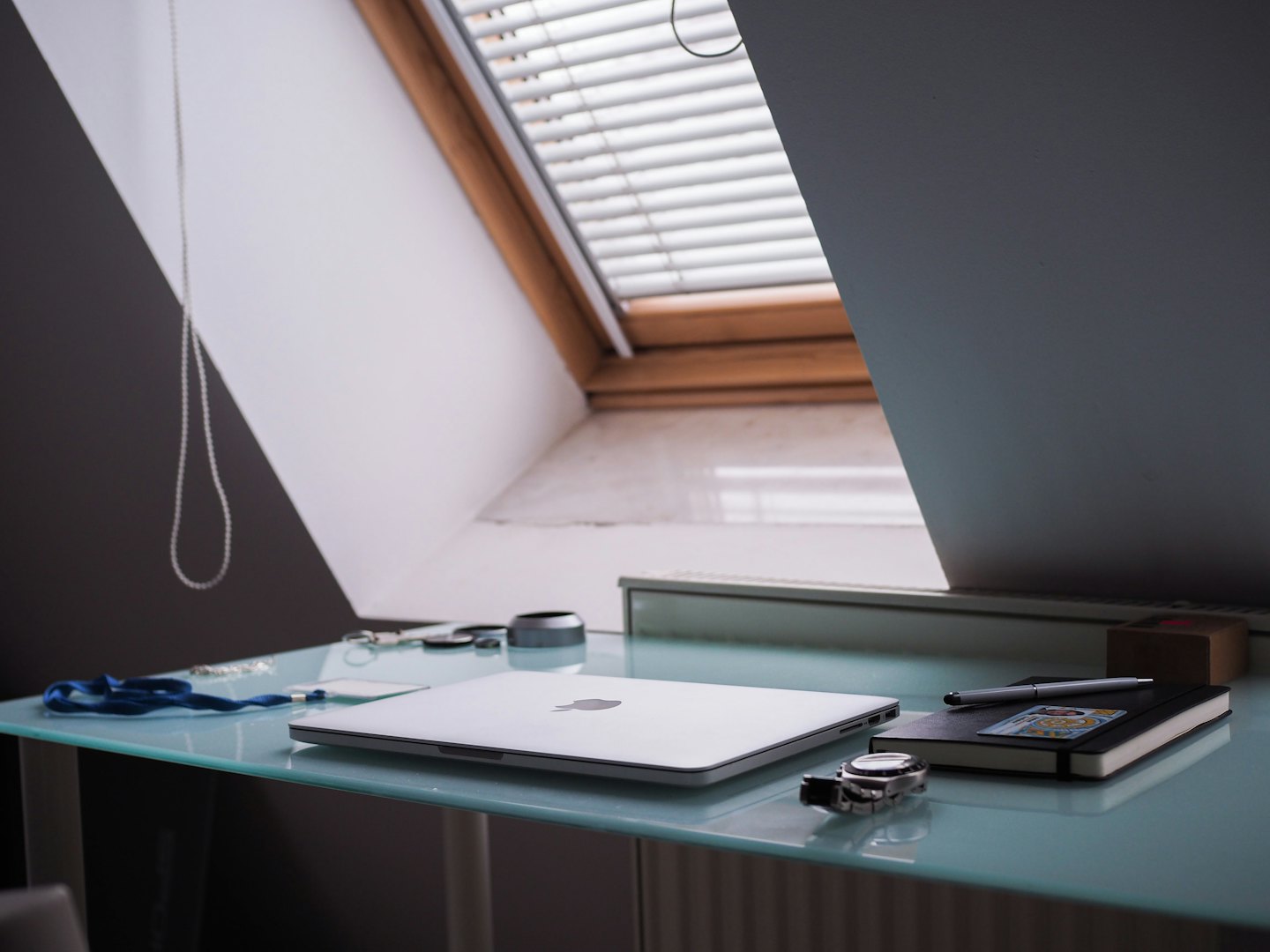 Modern home office with laptop, notebook, and pen on glass desk.