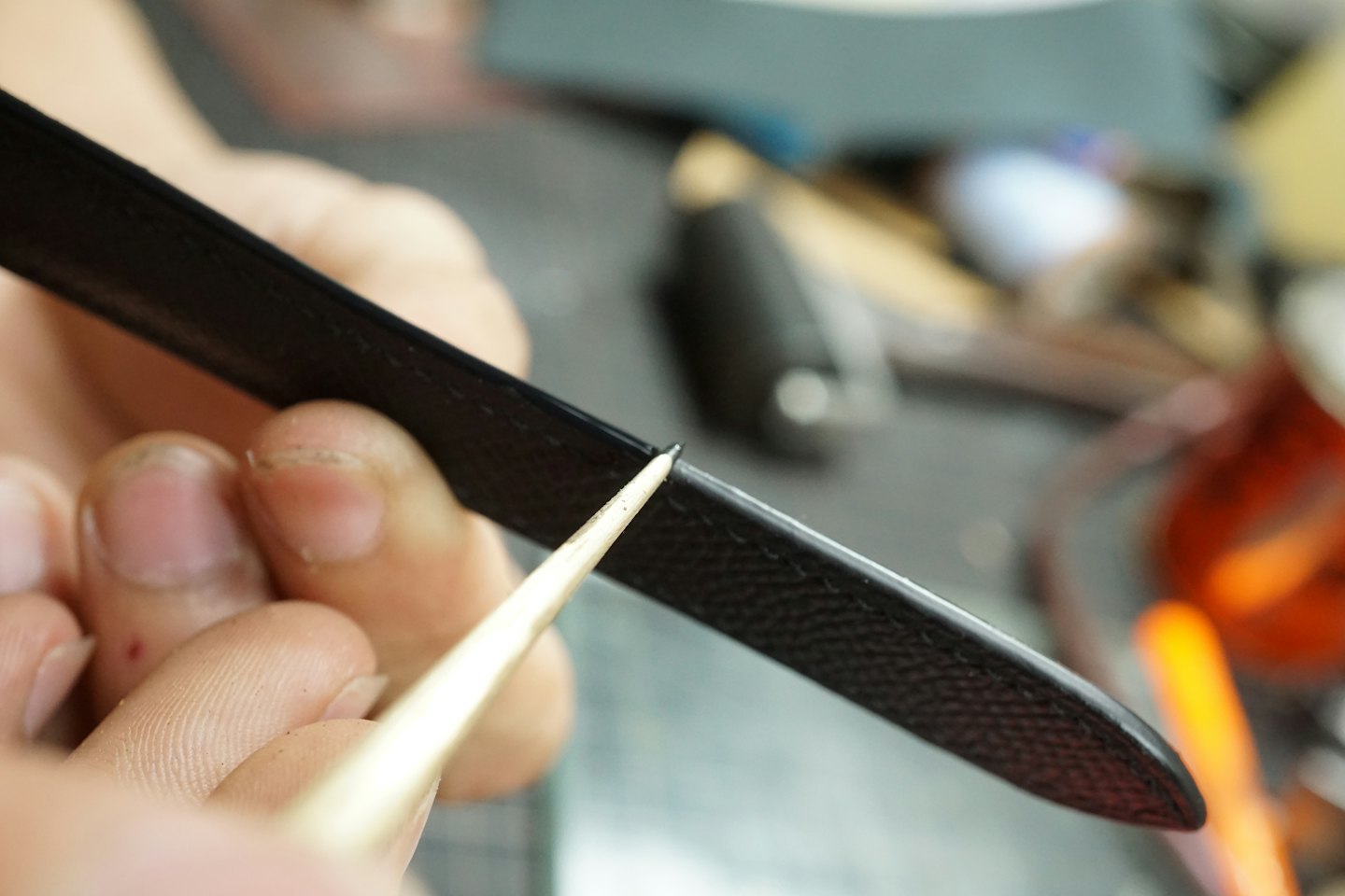 Hands use a tool to smooth the edge of leather.