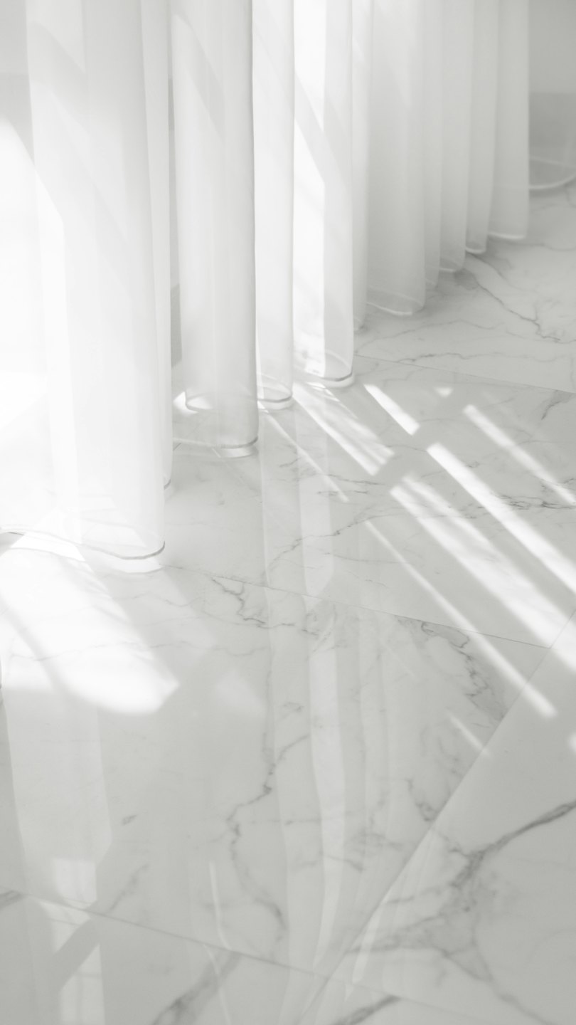 Sheer white curtains against a white marble floor.